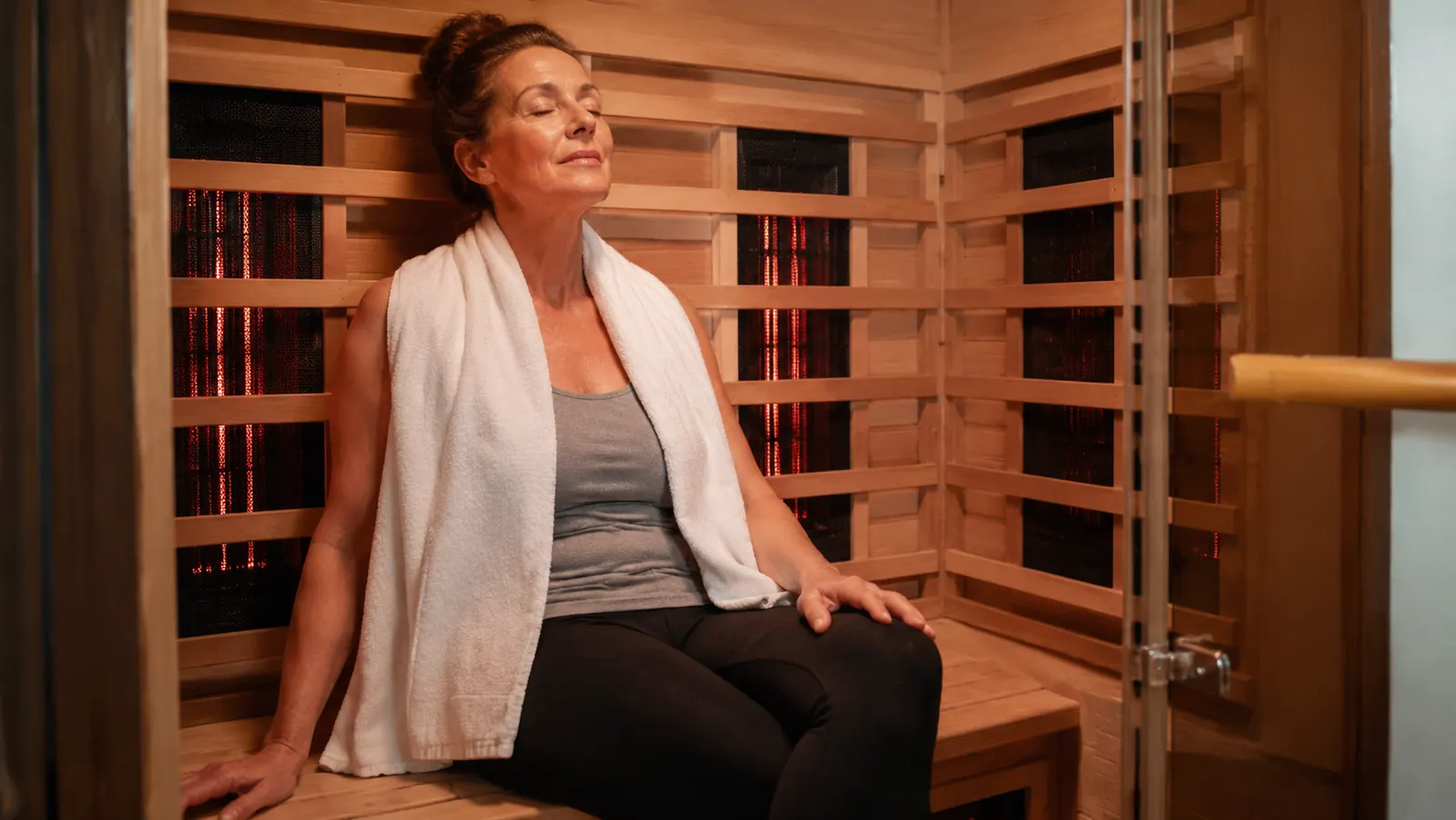 Person seated inside the Heat Wave cabin sauna on the interior bench with warm ambient light and a towel over their shoulders