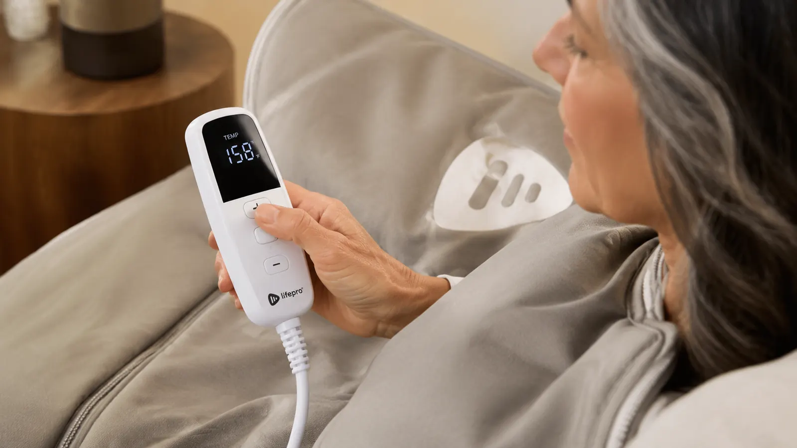 Close-up of a hand adjusting the temperature control unit clipped to the outside of the Lifepro RejuvaWrap