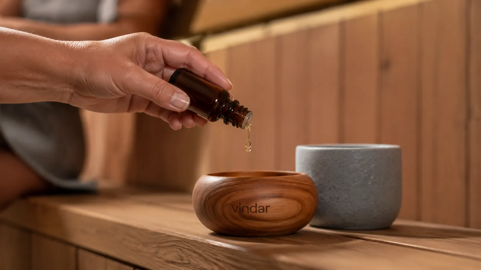 Hand adding drops of eucalyptus oil into the Vindar cedar bowl next to the stone cup for comparison