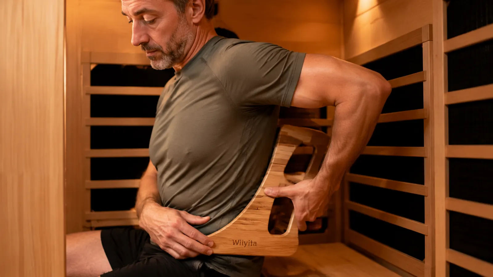 Person sitting upright on a sauna bench testing the placement of the Wiiyita Sauna Backrest against their lower back before a session